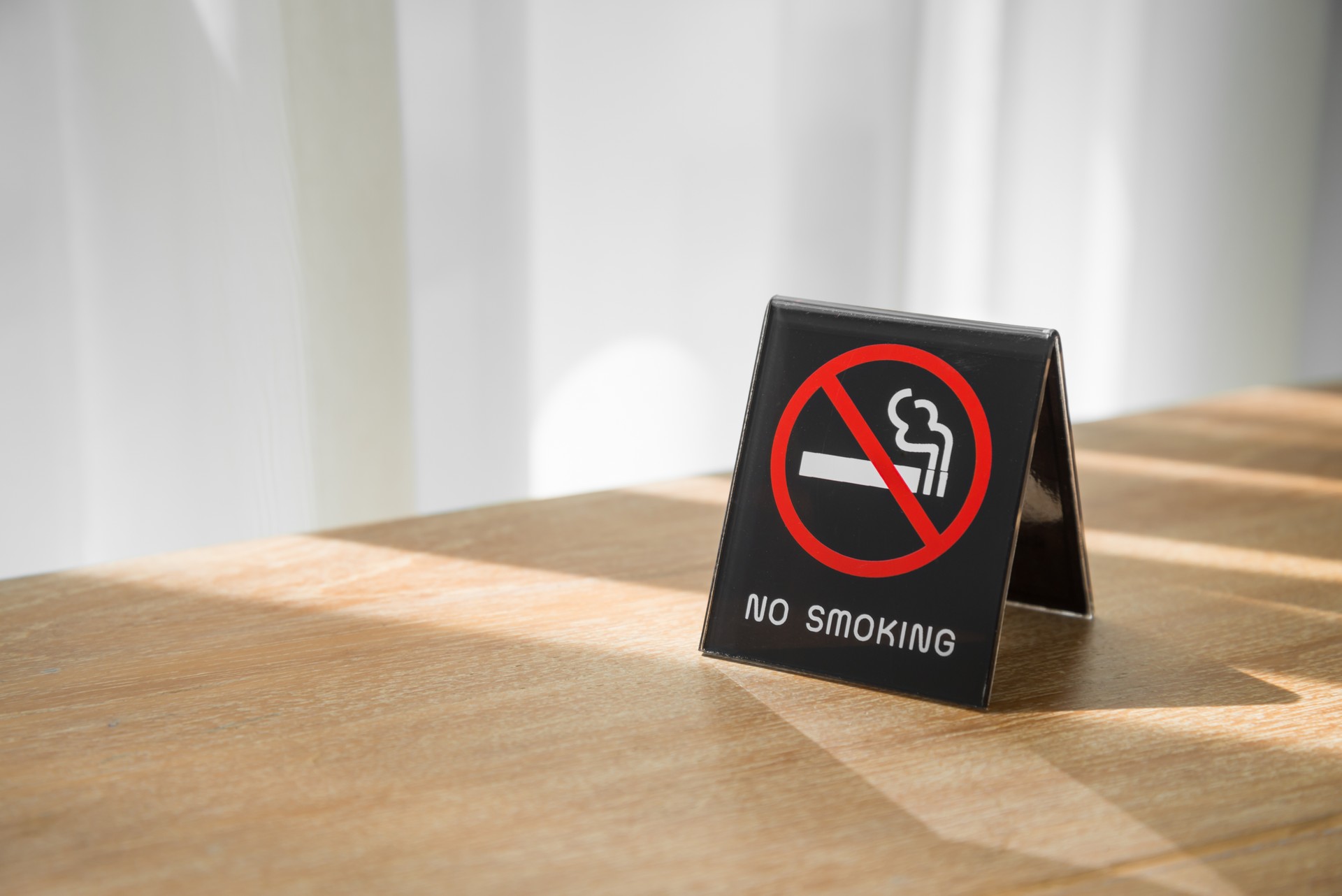 No smoking sign on table in hotel room with morning sunlight background.