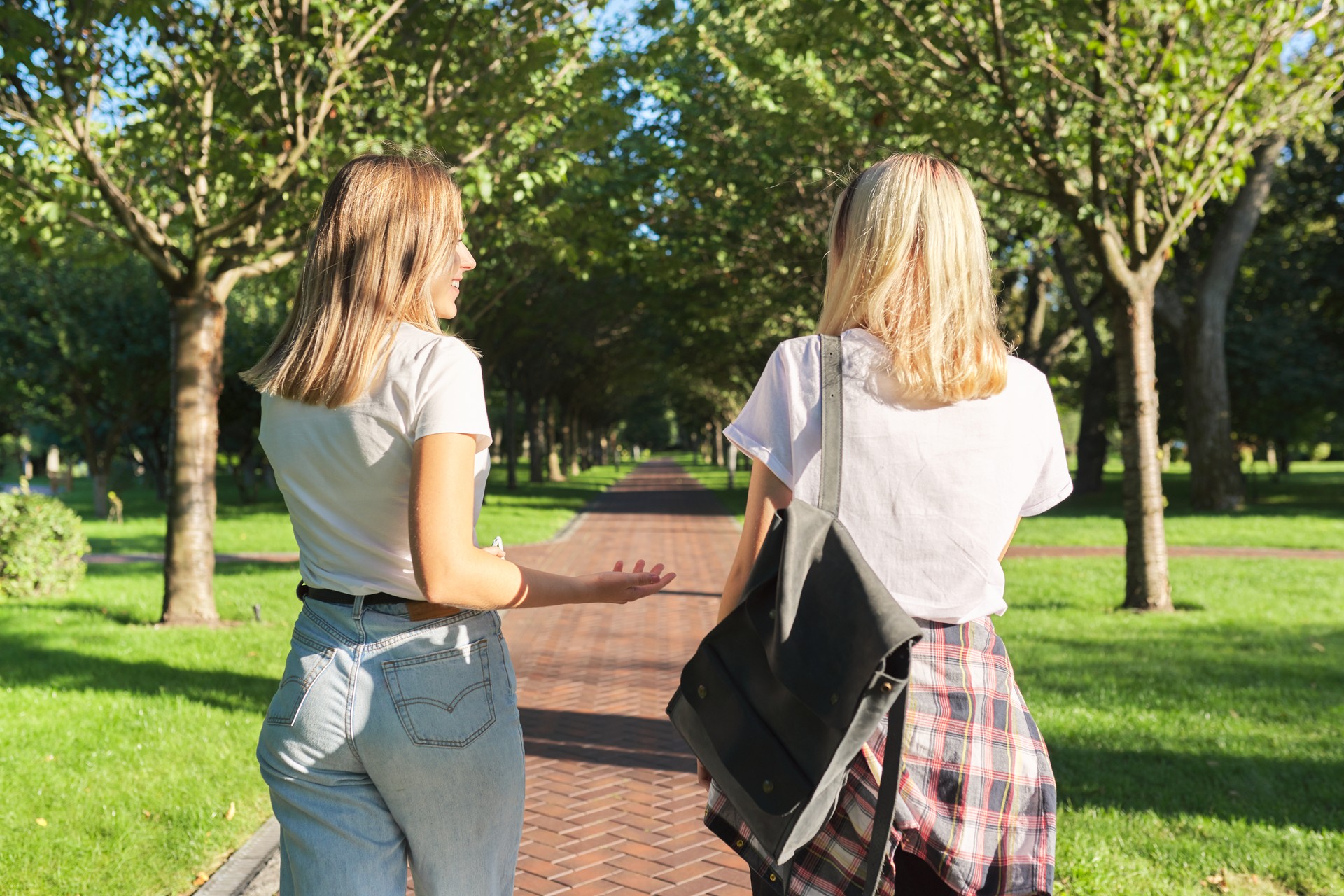 Two happy smiling talking girls teenagers students walking together, back view