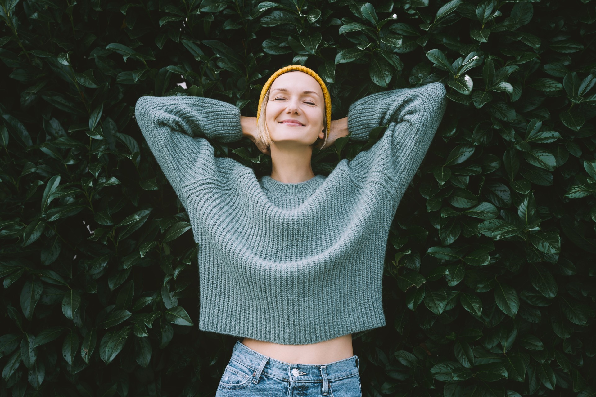 Portrait of relaxed and confident woman with eyes closed on background of green leaves wall. Thoughtful person in front of green hedge. Joy, zen and balance people. Stability through mental health